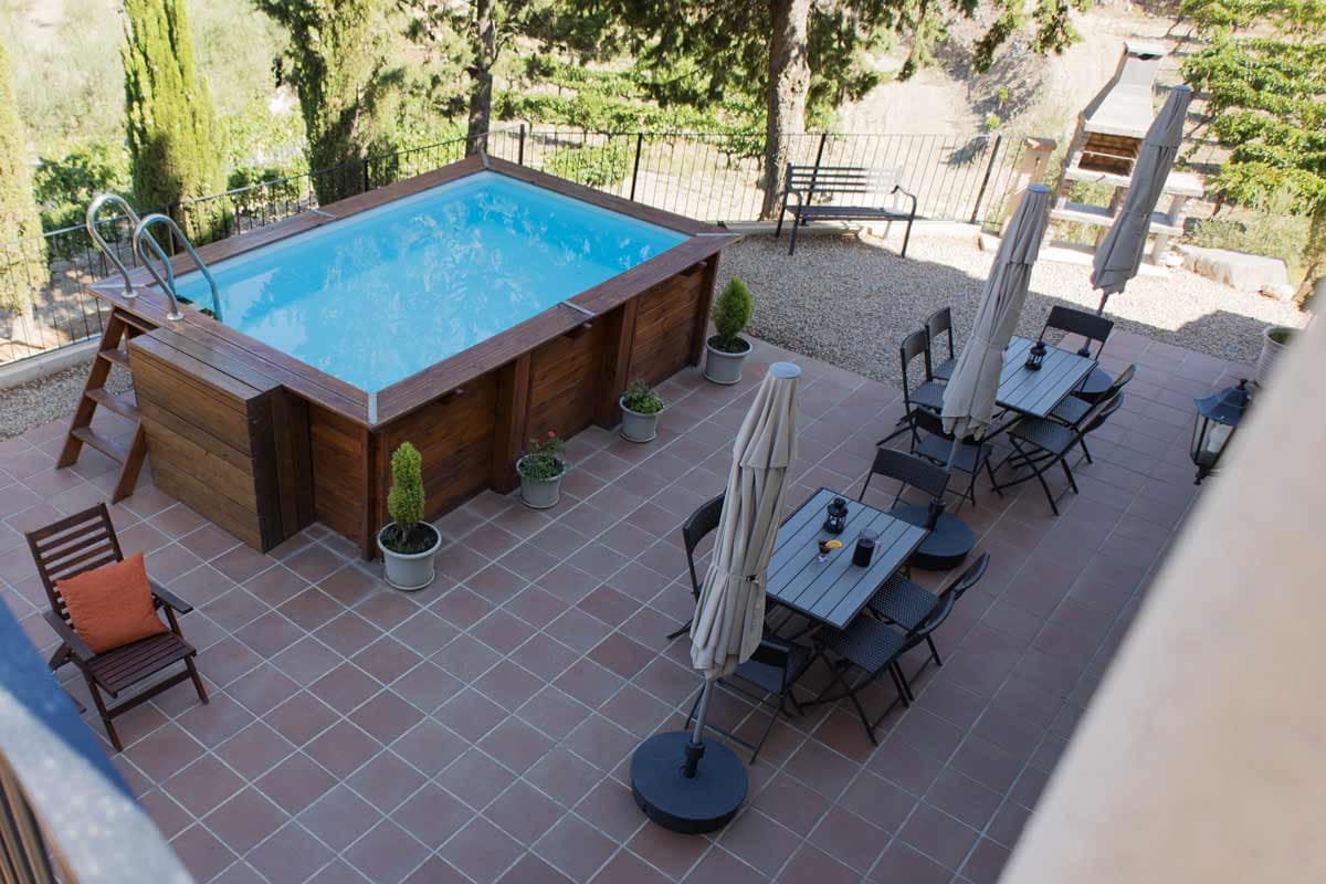 Terrace Terrassa on hi ha una barbacoa al fons, una piscina, unes gandules de fusta i taules i cadires amb para-sols, i una escala que puja a mà dreta.