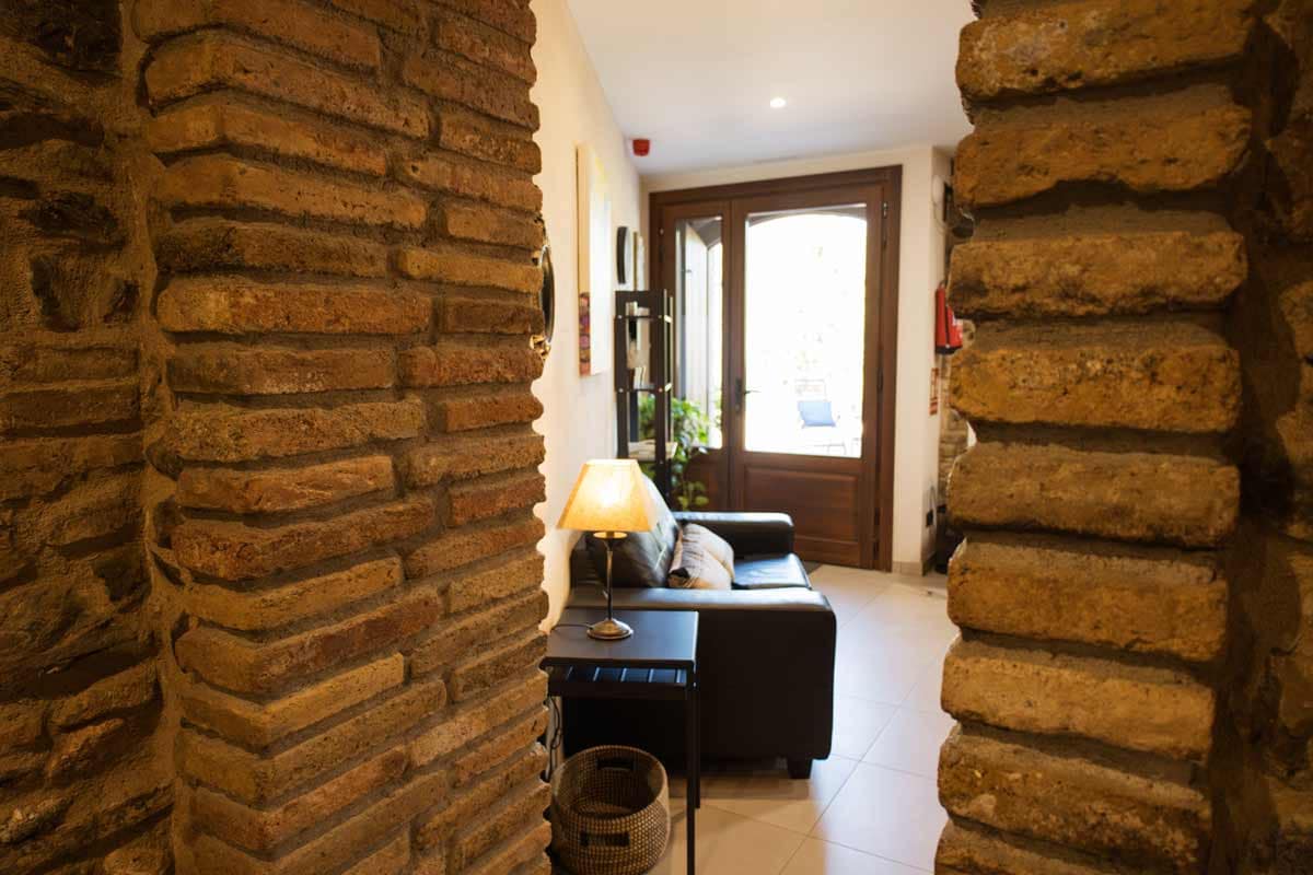 Entrance where you can see a wooden door and a glass that makes the street light, a black sofa, a tablet with a light and a black high furniture enter.