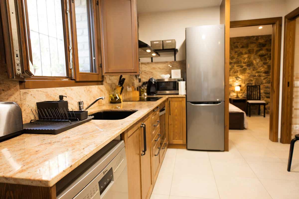 Fotografia general de la cuina on la paret és de pedra vista, on es veu una taula llarga de color negre, cadires del mateix color, una vitroceràmica, un llavaplats, una televisió, una nevera...