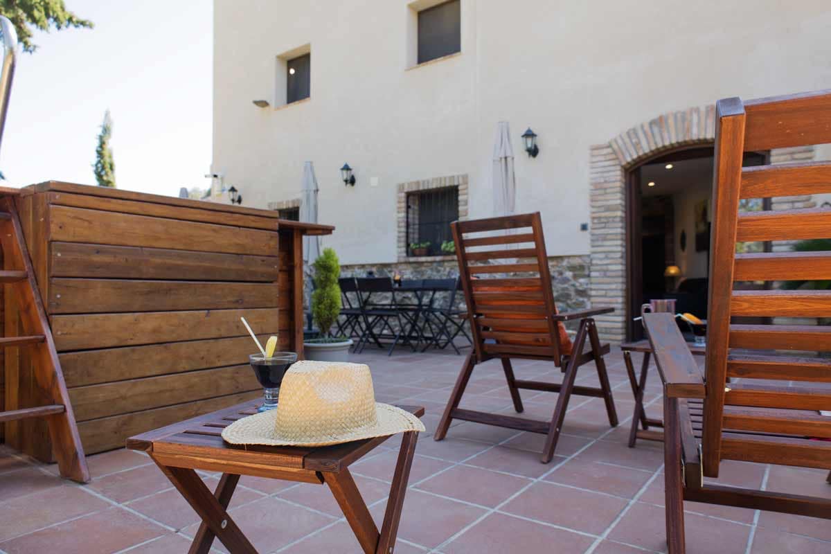 Terrace where there is a swimming pool, wooden loungers and tables and chairs with umbrellas.