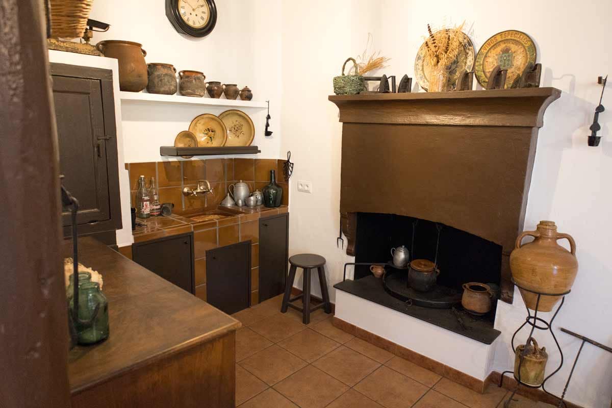 Kitchen with one fire on the ground, plates, ceramic pots, glass bottles, a round clock...