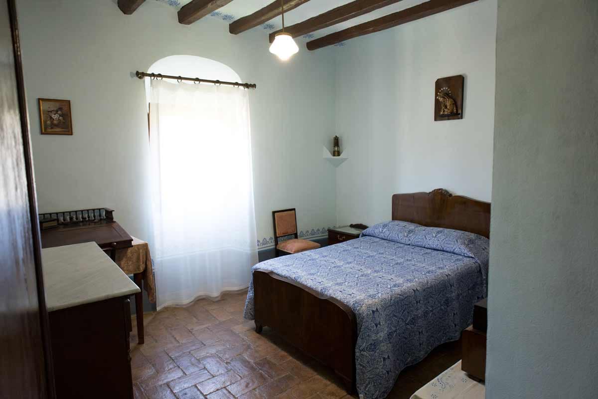 Double room with a bed in the middle and a picture in the center of the wall, a window where natural light enters, a chair, a night table...